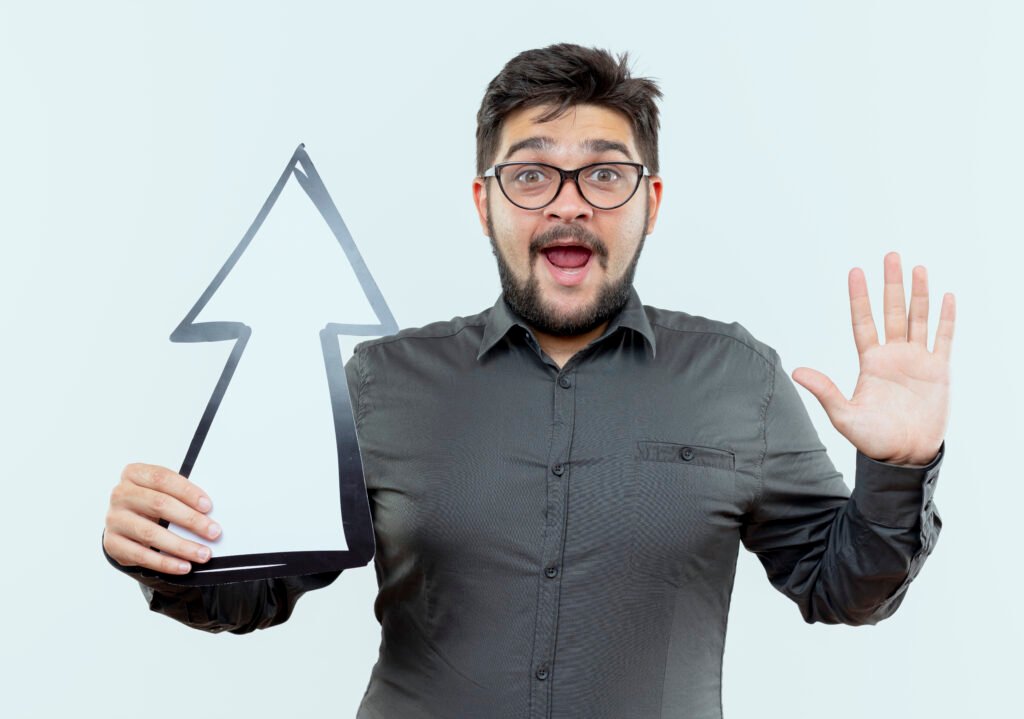 surprised young businessman wearing glasses holding direction mark and showing stop gesture isolated on white background
